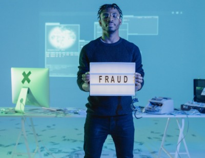 man standing on money holding a sign that says "fraud"