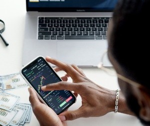 man looking at a graph on his phone with stacks of money in the background.