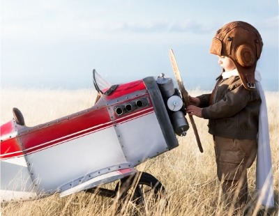 Toddler dressed as aviator with toddler sized plane.