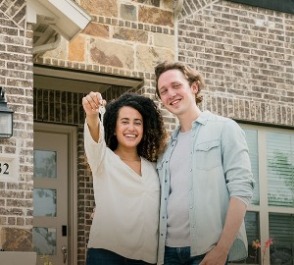 New homeowners holding keys in front of new house.