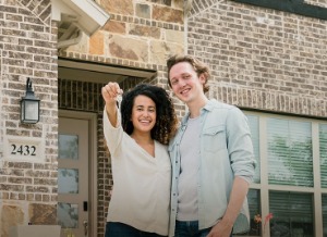 New homeowners holding keys in front of new house.