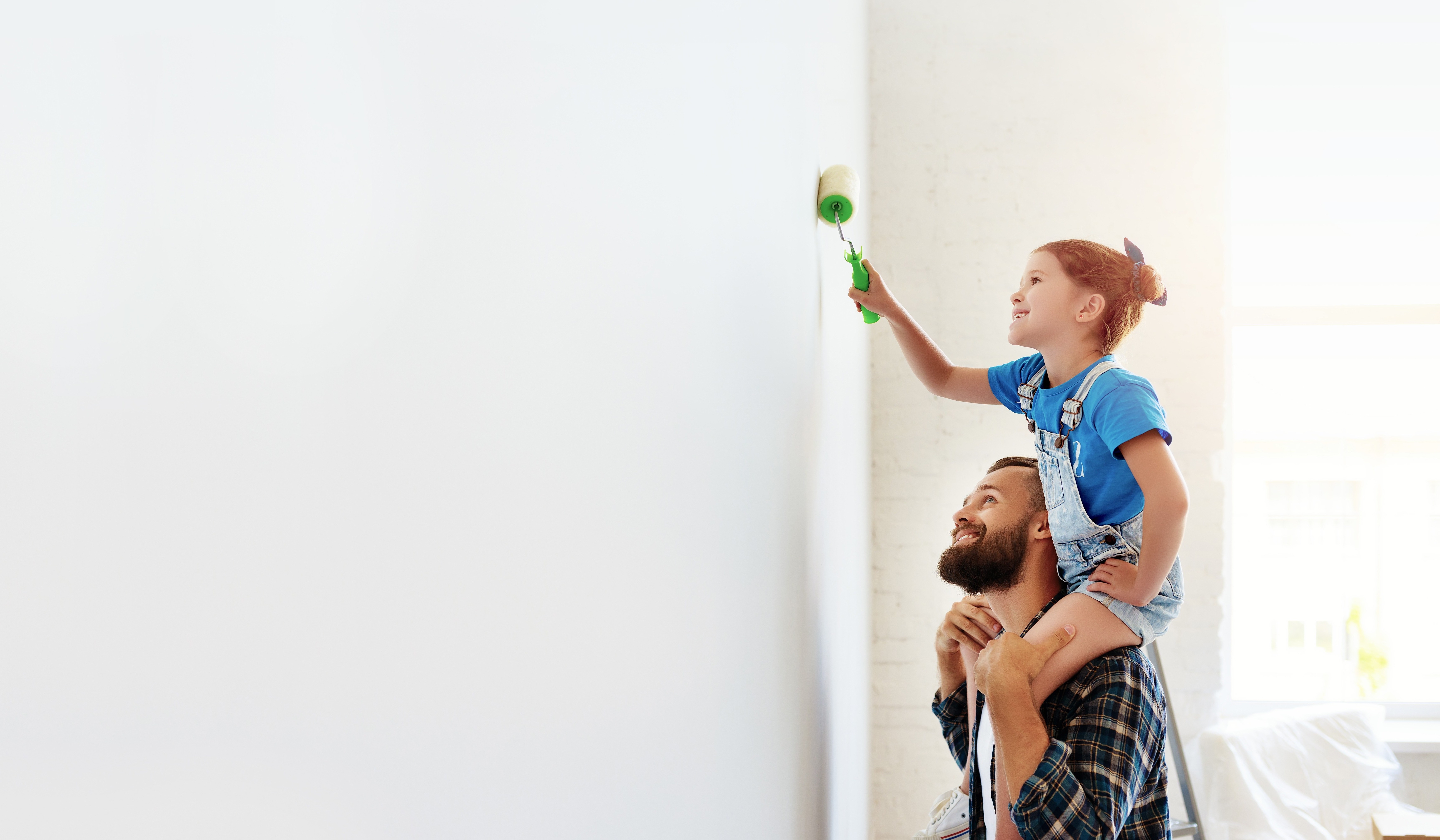 Girl sitting on father's shoulder painting a wall.