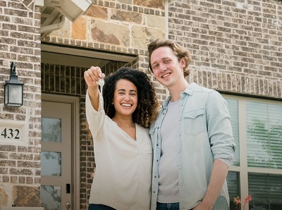 New homeowners holding keys in front of new house.