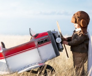 Toddler dressed as aviator with toddler sized plane.