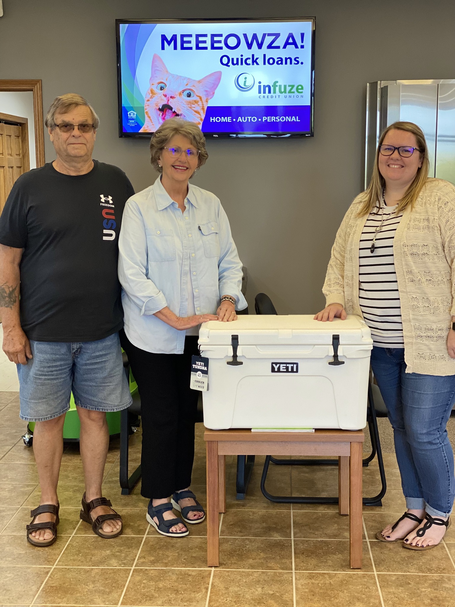 Two women and one man standing by ice chest.