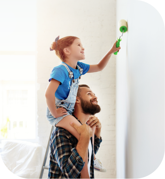 Girl sitting on father's shoulders painting a wall. 