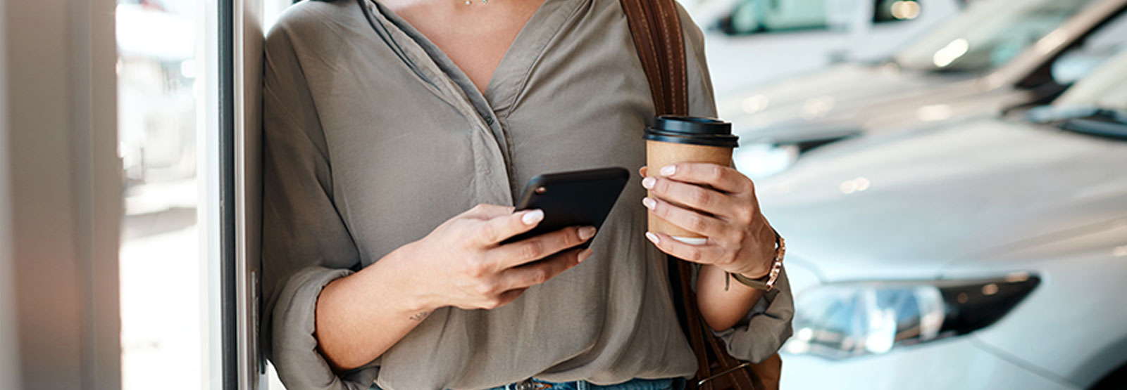 Woman checking auto insurance on phone at car dealership.