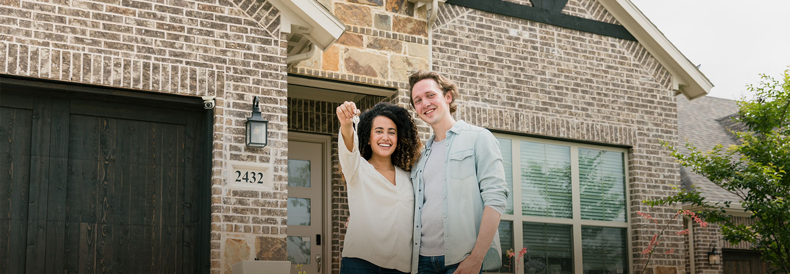 New homeowners holding keys in front of new house.