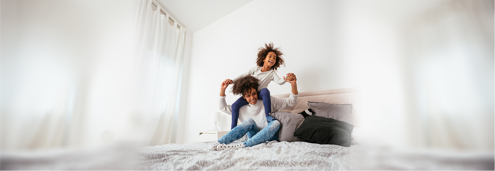 Woman sitting on bed with young girl on her shoulders.