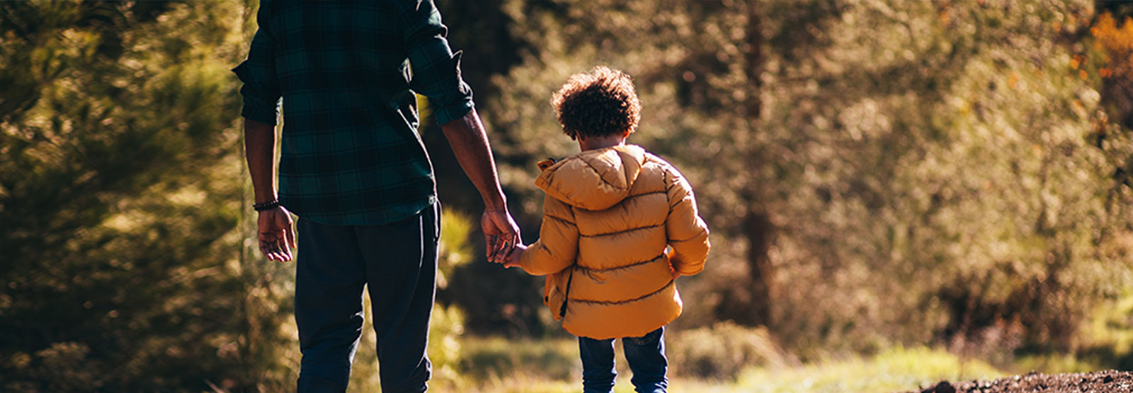 little kid holding their dad's hand while walking at a river