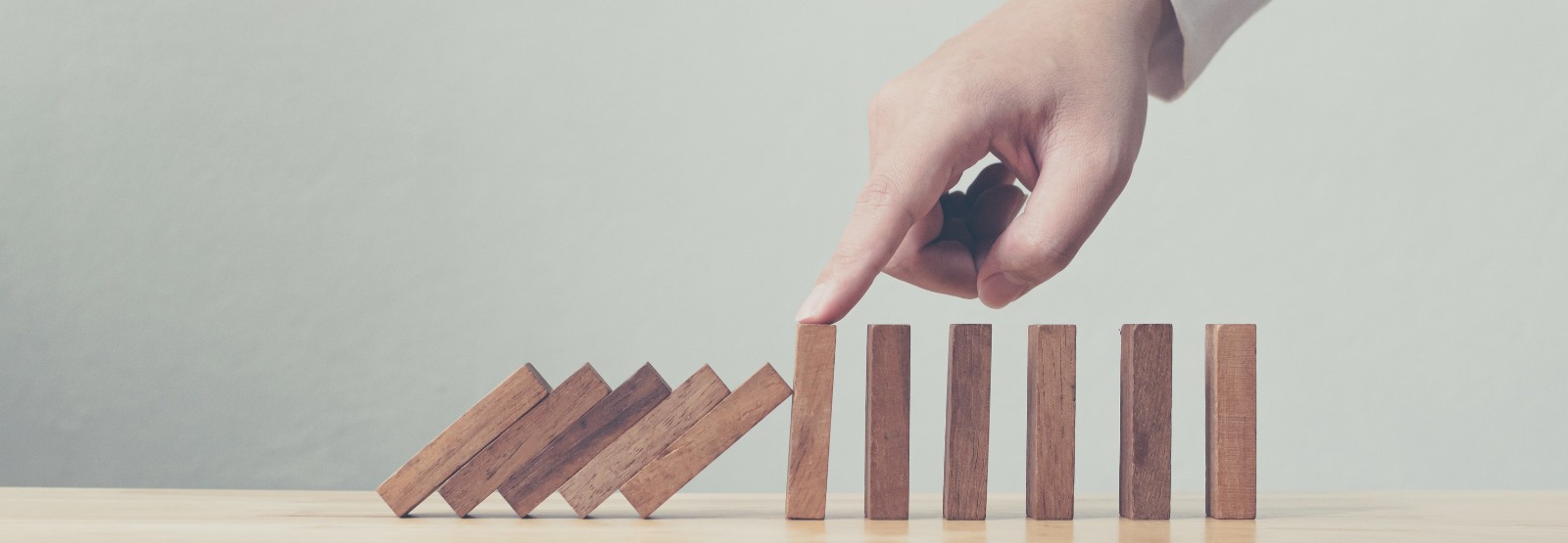 a finger stopping the collapse of wooden blocks