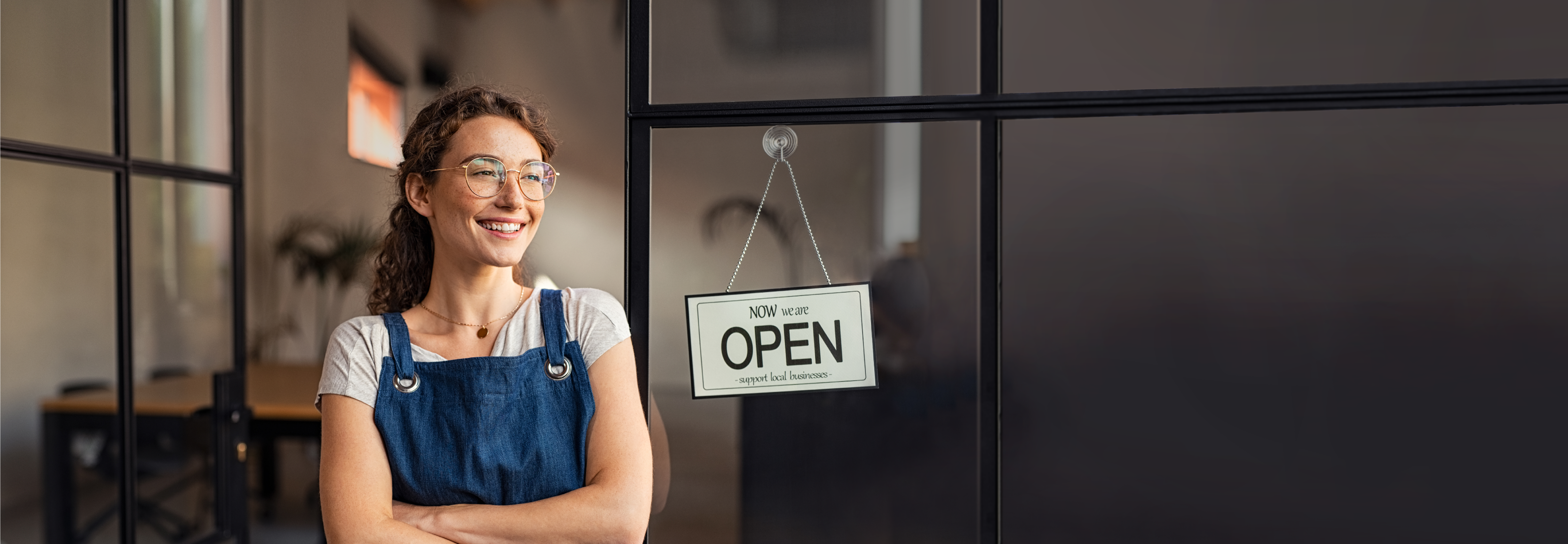 woman wearing an apron and smiling next to an open sign.