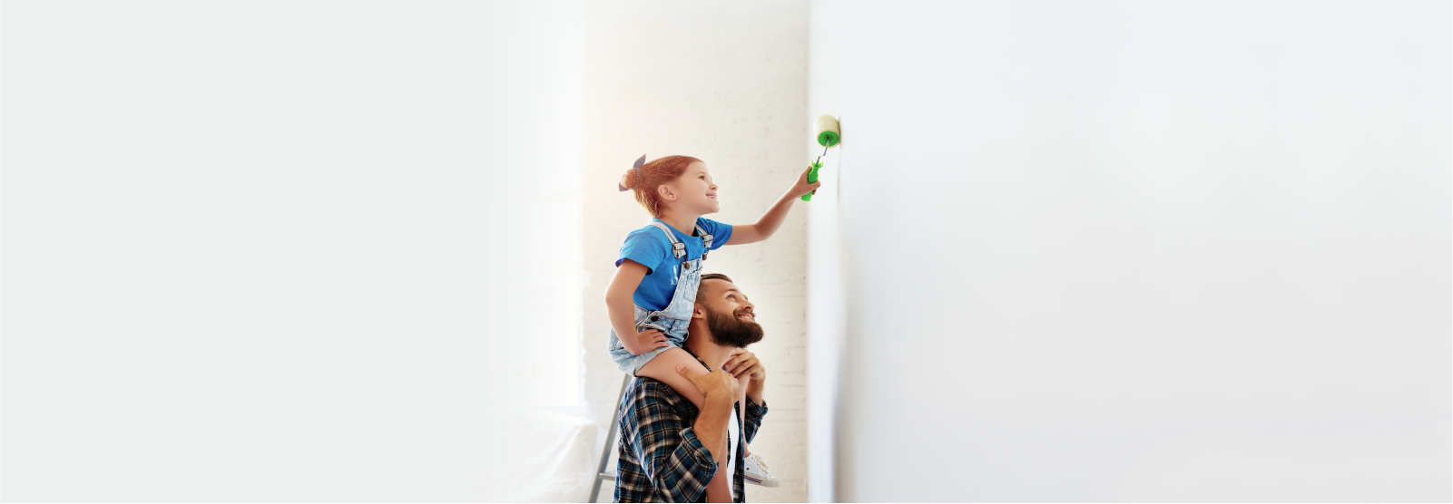 Girl on father's shoulders painting a wall. 