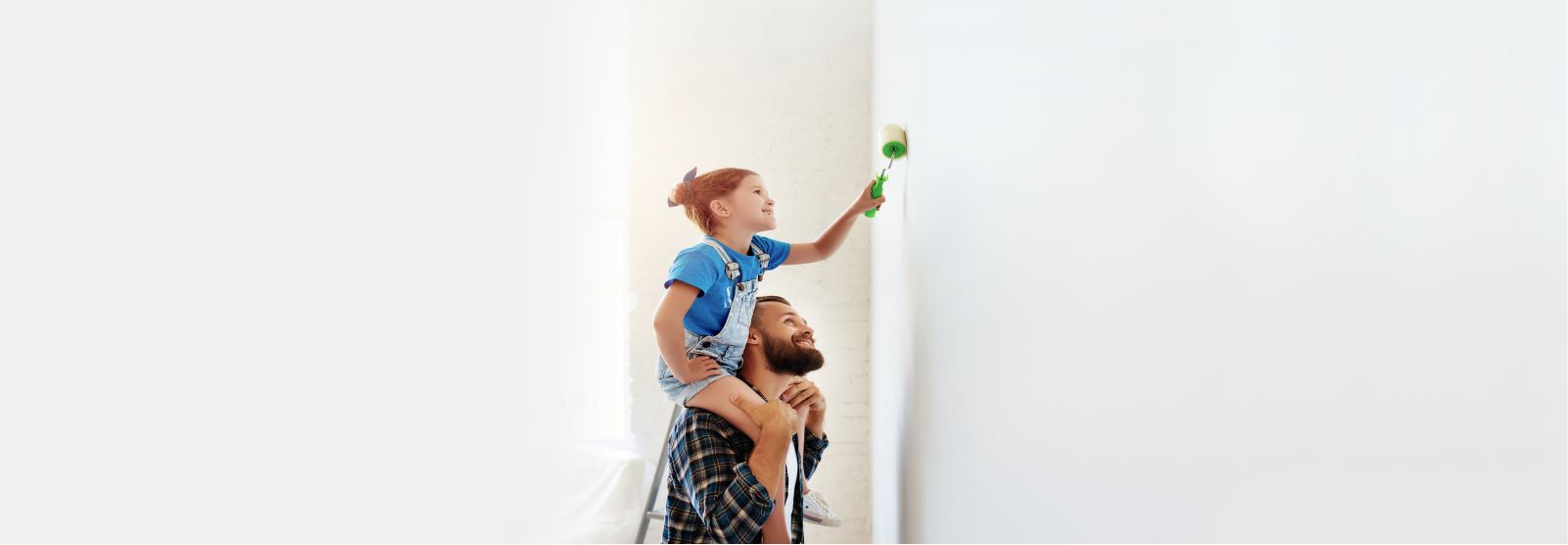 Girl on father's shoulders painting a wall.