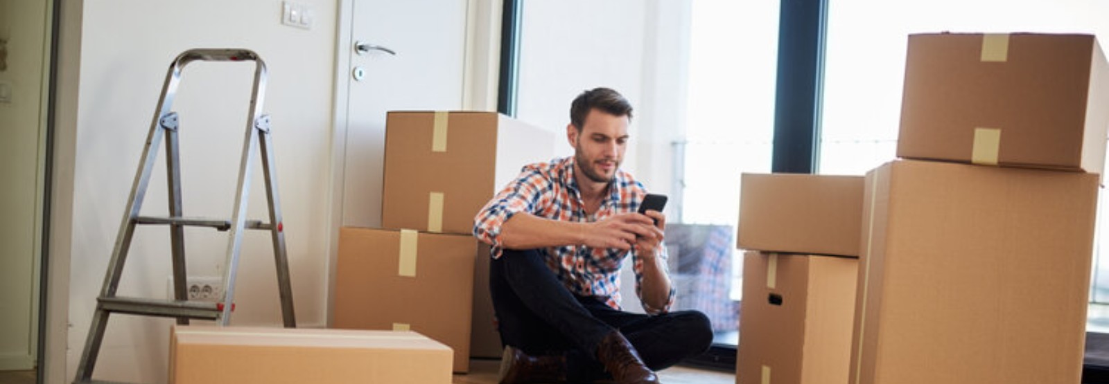 man looking at his smart phone in his new home surrounded by boxes