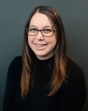 Portrait of a female smiling and wearing a black shirt and glasses.