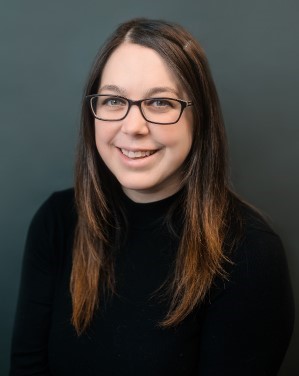 Portrait of a female smiling and wearing a black shirt and glasses. 