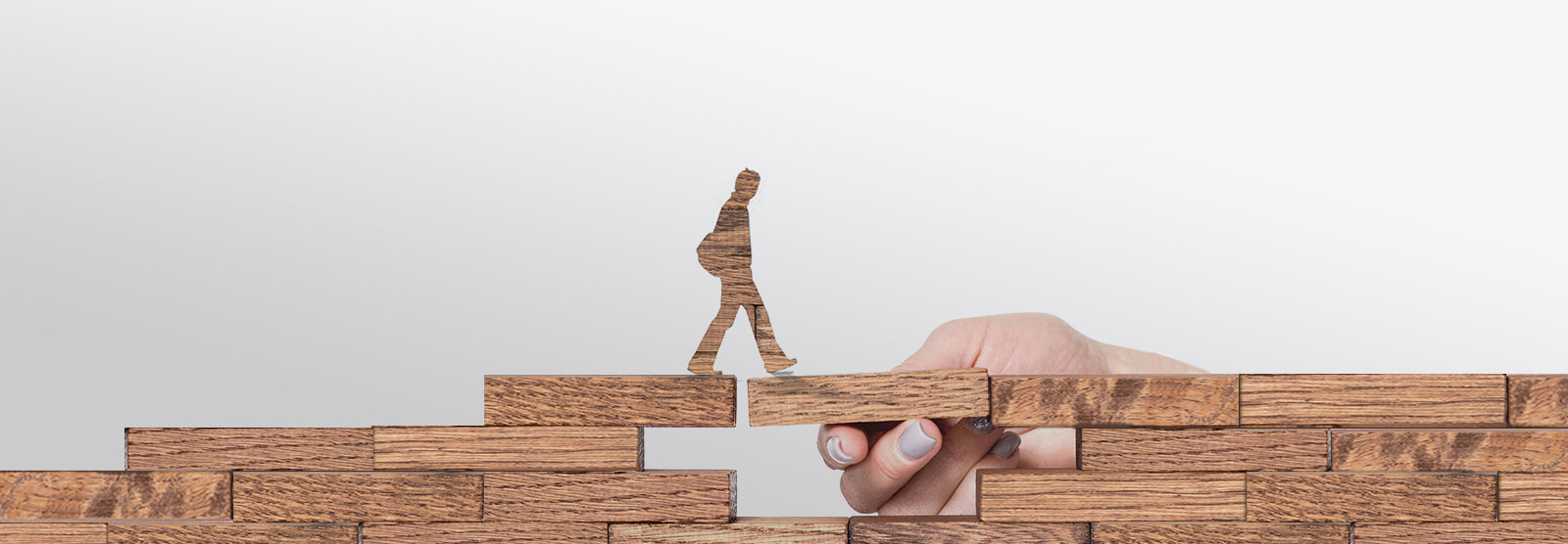 Wooden figure walking across wooden blocks held up by real hand.